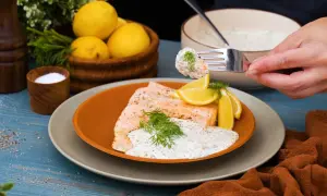 En bit lax med romsås, citronklyftor och dill. En gaffel med lax och sås lyfts från tallriken.