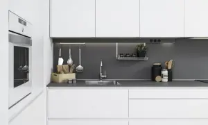 Moderna cocina blanca y gris con electrodomésticos integrados, fregadero de acero inoxidable y utensilios de cocina colgados.