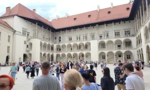 Tłum turystów zwiedza dziedziniec Wawelu, podziwiając renesansową architekturę. Warto zobaczyć na Wawelu to miejsce pełne historii.