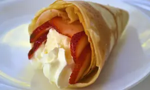 Délicieuse crêpe japonaise moelleuse garnie de fraises fraîches et de crème fouettée, servie sur une assiette blanche.