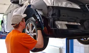Mechanik w czapce i pomarańczowej koszulce ogląda podniesiony czarny samochód.
