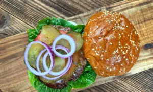 Burger z sałatą, ogórkiem, cebulą i wołowiną na desce drewnianej.