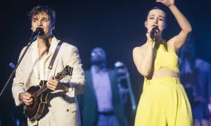 Młody mężczyzna gra na mandolinie, a kobieta śpiewa na scenie. Ich występ przypomina kwitnące kwiaty jabłoni na wiosennych koncertach.