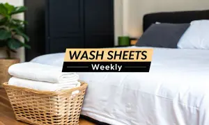 A clean bedroom with a neatly made bed. A basket of folded white towels sits beside the bed. Text overlay reads: "WASH SHEETS Weekly.