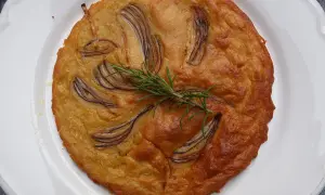 Herzhafte Kichererbsenmehl Rezepte: Goldbrauner Kuchen mit roten Zwiebeln und Rosmarin auf weißem Teller.