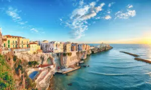 San Mennaio, un borgo sul mare con case colorate aggrappate alla scogliera, baciato dal sole al tramonto.
