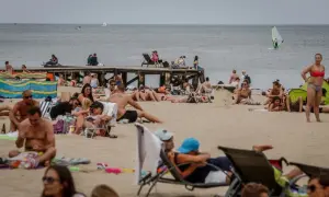 Tłum ludzi na plaży, opalanie się i relaks. Idealna pogoda na lipiec nad morzem, widać żaglówkę i wiatrak.