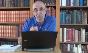 Un homme parle devant un ordinateur portable, entouré de livres. Il semble discuter de l'ad 07 état civil.