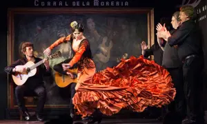 Una bailaora de flamenco, con un vestido naranja voluminoso, baila al son de guitarras. Es un espectáculo de flamenco vibrante.