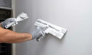 Mani guantate eseguono la rasatura di un muro con spatole cariche di stucco, preparando la superficie per la finitura.