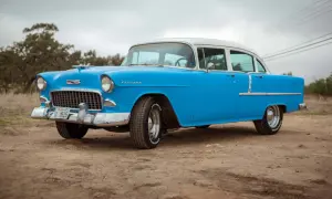 Blå och vit cheva 56 står parkerad på en grusväg. Bilen har kromade detaljer och vita däcksidor.