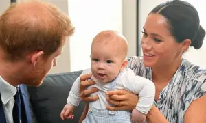 Meghan Markle trzyma swoje dziecko, które z zaciekawieniem patrzy na księcia Harry'ego.