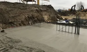 Budowa w toku: świeża wylewka betonowa na zewnątrz, zbrojenie i koparki w tle.