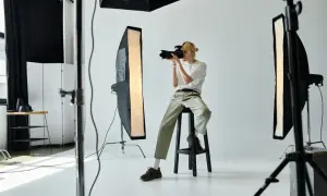 Młody fotograf w studiu, z aparatem w ręku, zastanawia się nad zawodem. Czy warto?