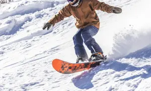 Mężczyzna na desce snowboardowej męskiej zjeżdża po ośnieżonym stoku, tworząc obłok śniegu.