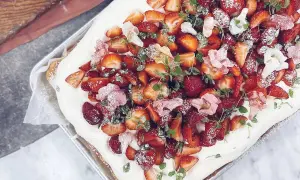 En midsommartårta i långpanna, täckt med fluffig grädde och generöst toppad med färska jordgubbar och små rosa blommor. Perfekt för sommarens firanden!