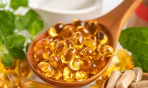 Łyżka pełna kapsułek z płynnym złotem – to suplementacja omega 3. Obok zielone liście i inne suplementy.