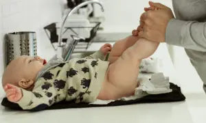 En bebis i pyjamas med björnar ligger på ett skötbord. En vuxen håller i bebisens ben. Det ser ut som att bebis pruttar mycket.
