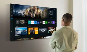 Mężczyzna patrzy na ekran telewizora Samsung Smart TV, gdzie wyświetlane są aplikacje i filmy. Dowiedz się, jak zaktualizować telewizor Samsung Smart TV, aby cieszyć się najnowszymi funkcjami.