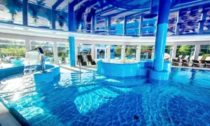 Relaks w spa nad morzem z basenem. Woda kaskadowo spływa do błękitnego basenu, a przez panoramiczne okna widać zieleń.