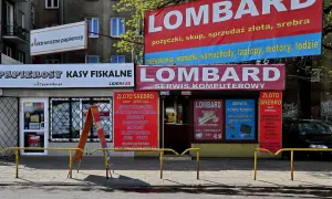Szyldy lombardu i sklepów z elektroniką i papierosami na tle budynku mieszkalnego.
