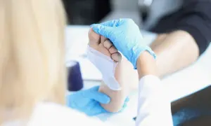 Dłoń w niebieskiej rękawiczce opatruje stopę, stosując opatrunek nasączony srebrem koloidalnym tonikiem.