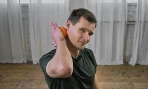 Mann lockert Nackenmuskulatur mit einer Orange.