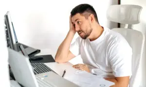 Zamyślony mężczyzna przy biurku z laptopami i dokumentami, zastanawia się, czy umowa zlecenie wlicza się do stażu pracy.