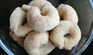 Un gruppo di taralli dolci, ricoperti di zucchero cristallino, in una ciotola di vetro.