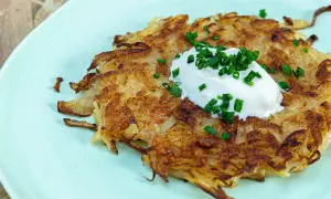 Une galette de pomme de terre dorée et croustillante, garnie d'une cuillère de crème fraîche et de ciboule ciselée. Un délice simple et savoureux.