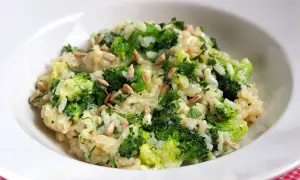 Kremowe risotto z brokułami, posypane słonecznikiem i natką pietruszki, podane w białej misce.