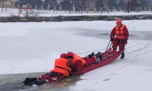 Ratownicy w akcji, wyciągają osobę z lodowatej wody za pomocą **sanki ratownicze**. Zimowa sceneria i profesjonalny sprzęt.