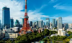 Tokio Tower góruje nad nowoczesnym miastem z wieżowcami w budowie i zielonymi drzewami.