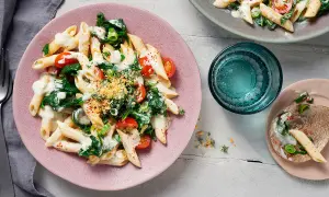 Penne mit Spinat und cremiger Sauce auf einem rosa Teller, garniert mit Kirschtomaten und Kräutern.