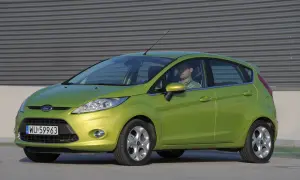 Zielony Ford Fiesta Mk7 z widocznymi żarówkami z przodu, zaparkowany przed budynkiem.