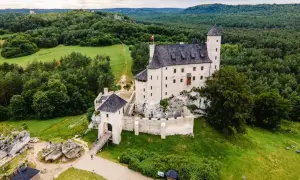 Zamek Bobolice, malowniczo położony na skale, otoczony zielenią i lasami.