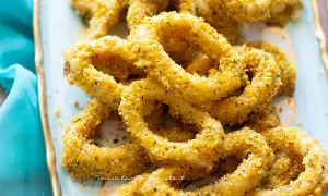 Anelli di totano al forno, dorati e croccanti, serviti su un piatto azzurro con un tovagliolo turchese.