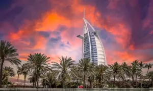 Zachód słońca nad Dubajem z palmami i hotelem Burdż al-Arab. Zastanawiasz się, ile kosztuje wycieczka do Dubaju?