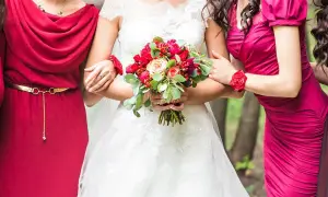 Panna młoda z bukietem czerwonych kwiatów, otoczona przez druhny w sukniach w odcieniach czerwieni i fuksji. Kolory te mogą być inspiracją, jakich kolorów nie ubierać na wesele, by nie przyćmić panny młodej.