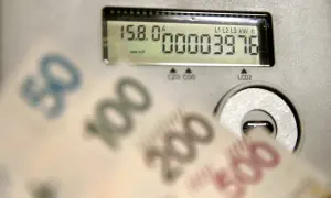 Cyfrowy licznik energii pokazuje zużycie, a przed nim rozmazane banknoty 50, 100, 200 i 500 zł. Rachunek za prąd może być wysoki.