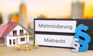 Hausmodelle, Waage der Gerechtigkeit und Ordner mit "Mietminderung" und "Mietrecht" – ein Symbol für die Bewertung von Wasserschäden.