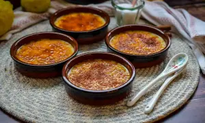 Vier Crema Catalana Schalen mit karamellisierter Zuckerkruste, bereit für das Crema Catalana Rezept. Zitronen und Löffel liegen daneben.