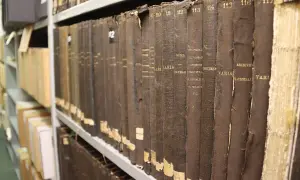 Rangées de vieux registres reliés en tissu brun dans les archives départementales 85. Les titres sont partiellement lisibles.