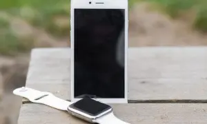 Biały smartwatch i smartfon leżą na drewnianym stole. Dowiedz się, jak sparować zegarek z telefonem, by cieszyć się nowymi możliwościami.
