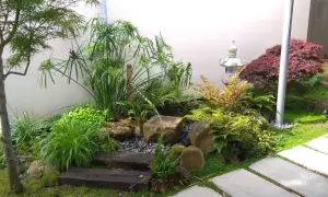 Un sereno mini jardín japonés en casa, con cascada de agua, rocas, plantas exuberantes y una linterna de piedra.