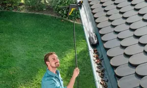 Hombre sonriente usando un accesorio para limpiar canalones altos con una hidrolimpiadora.