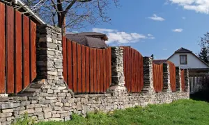 Solidne ogrodzenie z cegły i drewna, z kamiennymi słupkami, tworzy stylową barierę dla domu.