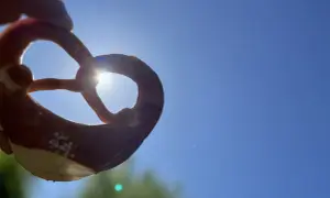 Ein Brezel wird gegen die Sonne gehalten. Woher kommen Brezeln? Aus dem Teig, der zu dieser Form geknetet wird.