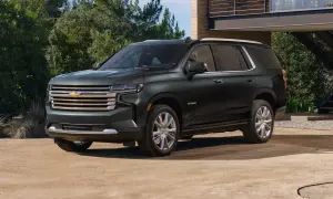 Ciemnozielony Chevrolet Tahoe High Country z chromowanymi felgami stoi przed nowoczesnym domem.