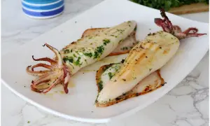 Due calamari alla griglia, conditi con erbe aromatiche, serviti su un piatto bianco.